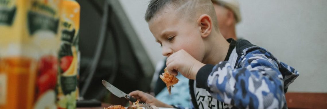 Young boy savoring a grilled chicken meal during an outdoor barbecue.